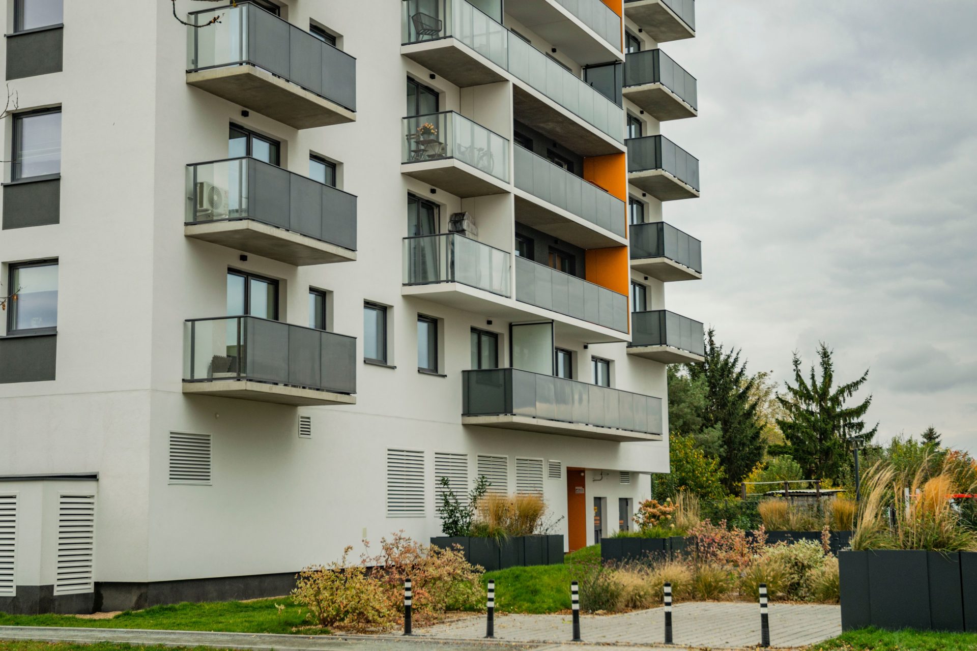 Moderner Apartmentkomplex mit Glasbalkonen und landschaftlich gestalteter Umgebung.